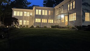 Uma casa de dois andares com várias janelas e fachada bem iluminada ao entardecer.