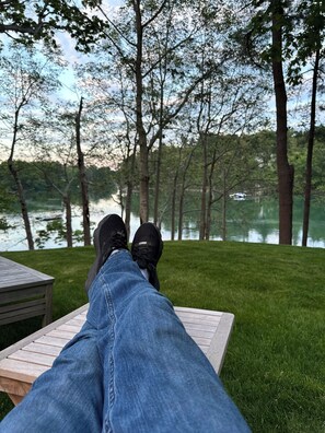 A person's legs and feet resting on a wooden bench with a view of a lake and trees in the background. - the orchards restored mansion over 10,000 sq ft on 6 acres on the york river. (York)