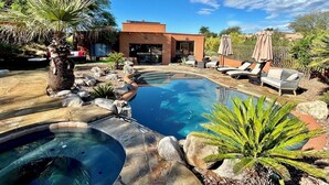 Zwembad met een jacuzzi, omringd door rotsen en planten, en een gebouw met terras op de achtergrond.