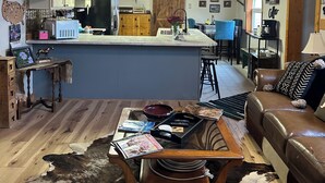 A cozy living room with a wooden ceiling, a central island with bar stools, a brown leather couch, and a cowhide rug.