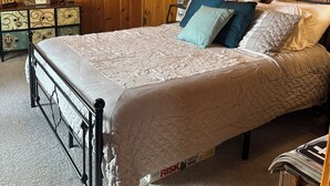 A wooden-paneled bedroom with a bed, a nightstand, a lamp, and framed pictures on the walls.