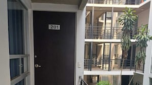 A balcony with a door marked '201,' a metal railing, and a view of a multi-story building with balconies and potted plants.