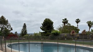 Une piscine entourée d’une clôture, avec une pelouse et des arbres.