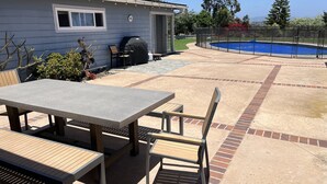 Un jardin avec une table et des chaises de patio, un barbecue et une piscine.
