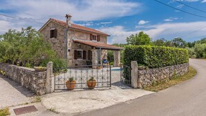 A stone house with a tiled roof, a stone wall, and a metal gate with potted plants.