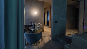 A modern interior with a dining area featuring a round table and a blue chair, a pendant light, and a staircase leading to an upper level. - GOLD SUITE&SPA (Palermo)