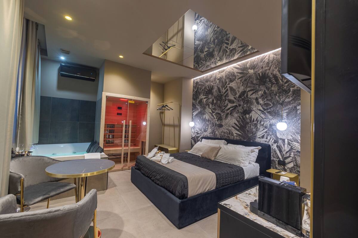 Quarto de hotel moderno com uma cama grande, um espaço de estar com uma mesinha, uma banheira e uma obra de arte na parede.