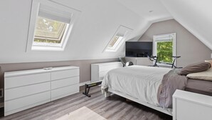 A bedroom with a sloped ceiling, skylight windows, a bed, a dresser, a mirror, and a bicycle. - Springs / Amagansett area. Walk to bay. Private / 4 bedrooms  (East Hampton)