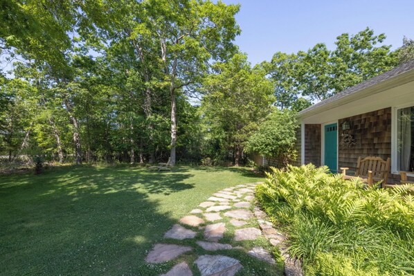 A house with a stone pathway leading to a green lawn surrounded by trees.