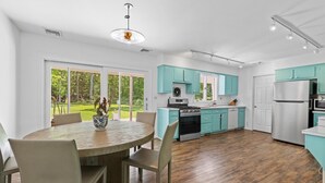A modern kitchen with teal cabinets, a central island, and a dining area with a round table and chairs. - Springs / Amagansett area. Walk to bay. Private / 4 bedrooms  (East Hampton)