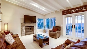 A spacious living room with a fireplace, leather sofas, and large windows offering a view. - Villa Solamar-Sunset Cliffs Spectacular (San Diego)