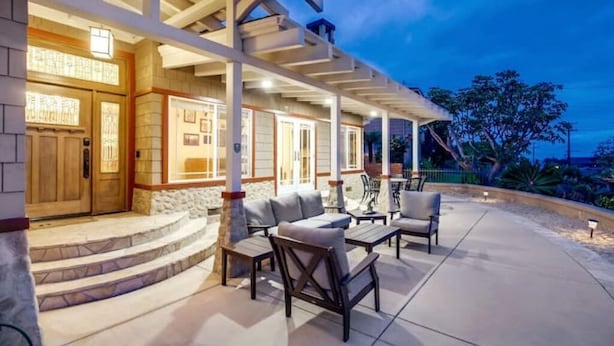 A covered outdoor seating area with stone steps leading to a wooden door, furnished with sofas and tables. - Villa Solamar-Sunset Cliffs Spectacular (San Diego)