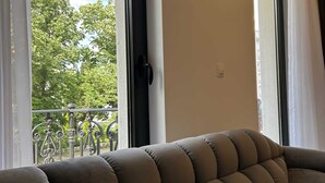 En balkong med en bekväm sittplats, utsikt över träd och byggnader samt ett räcke.