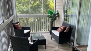 Une véranda aménagée avec des meubles en osier, une table en verre et une plante en pot.