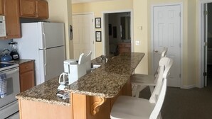 Une cuisine dotée de plans de travail en granit, d’armoires en bois, d’un réfrigérateur et d’une machine à café.