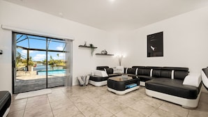 Ein modernes Wohnzimmer mit einem großen Schiebeglasfenster zum Pool, einem schwarz-weißen Ecksofa und einem Couchtisch.