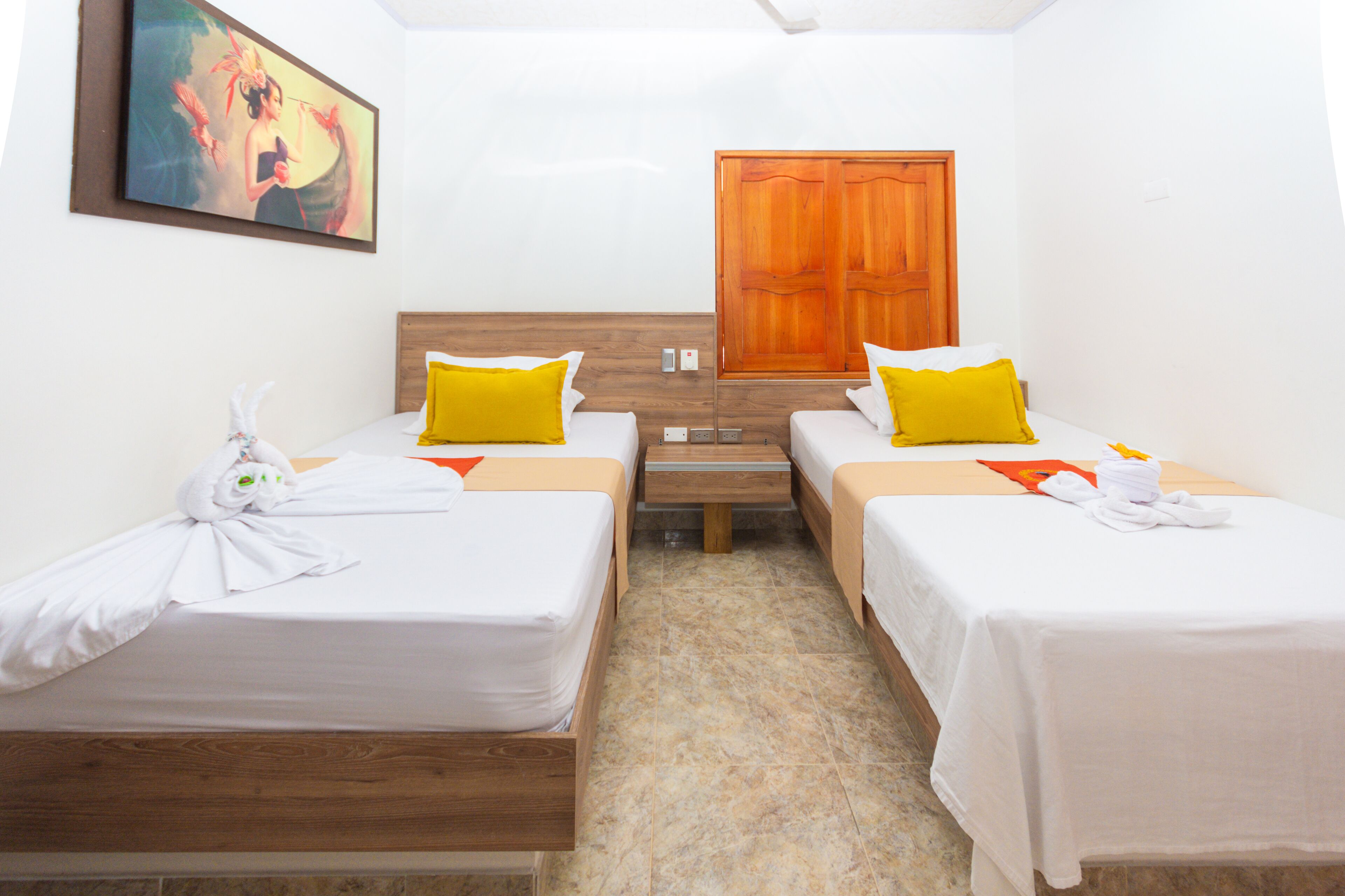 A hotel room with two single beds, a wooden headboard, a wooden door, and a painting on the wall.