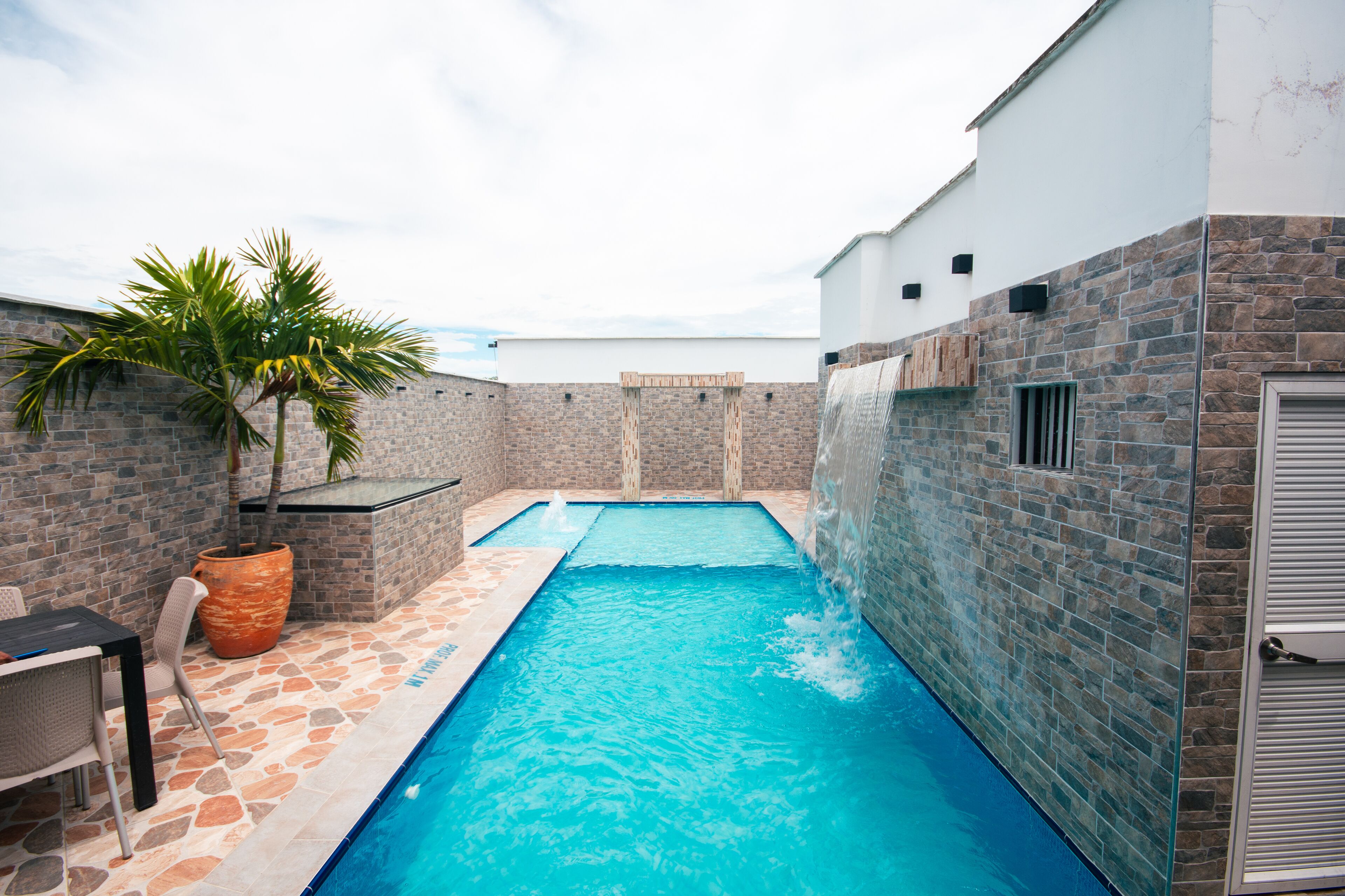 A swimming pool with a stone and brick exterior, a table with chairs, and a potted plant.