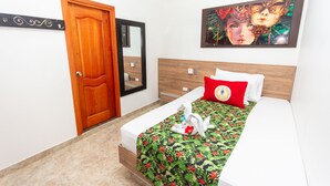 Ein Hotelzimmer mit Holztür, einem Bett mit floralem Überwurf, einem roten Kopfkissen und einem Bild an der Wand.