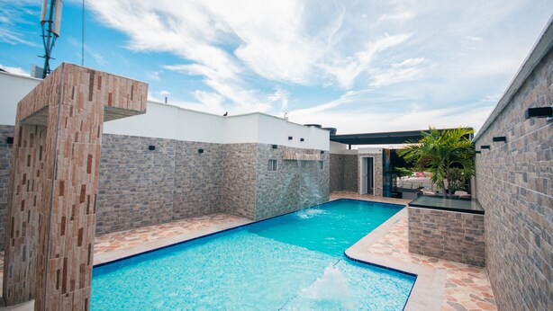 Ein Pool mit Stein- und Fliesenbordur, einer Ziegelwand und blauem Himmel.