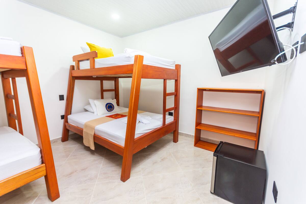 Une chambre avec un lit superposé, un téléviseur fixé au mur et une petite étagère.