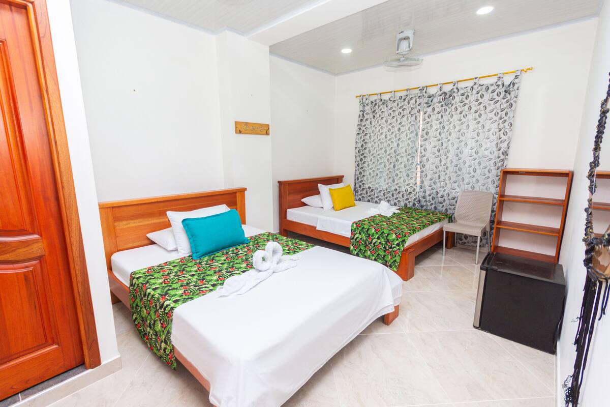 Une chambre d’hôtel avec deux lits, un bureau, une chaise et un petit réfrigérateur.