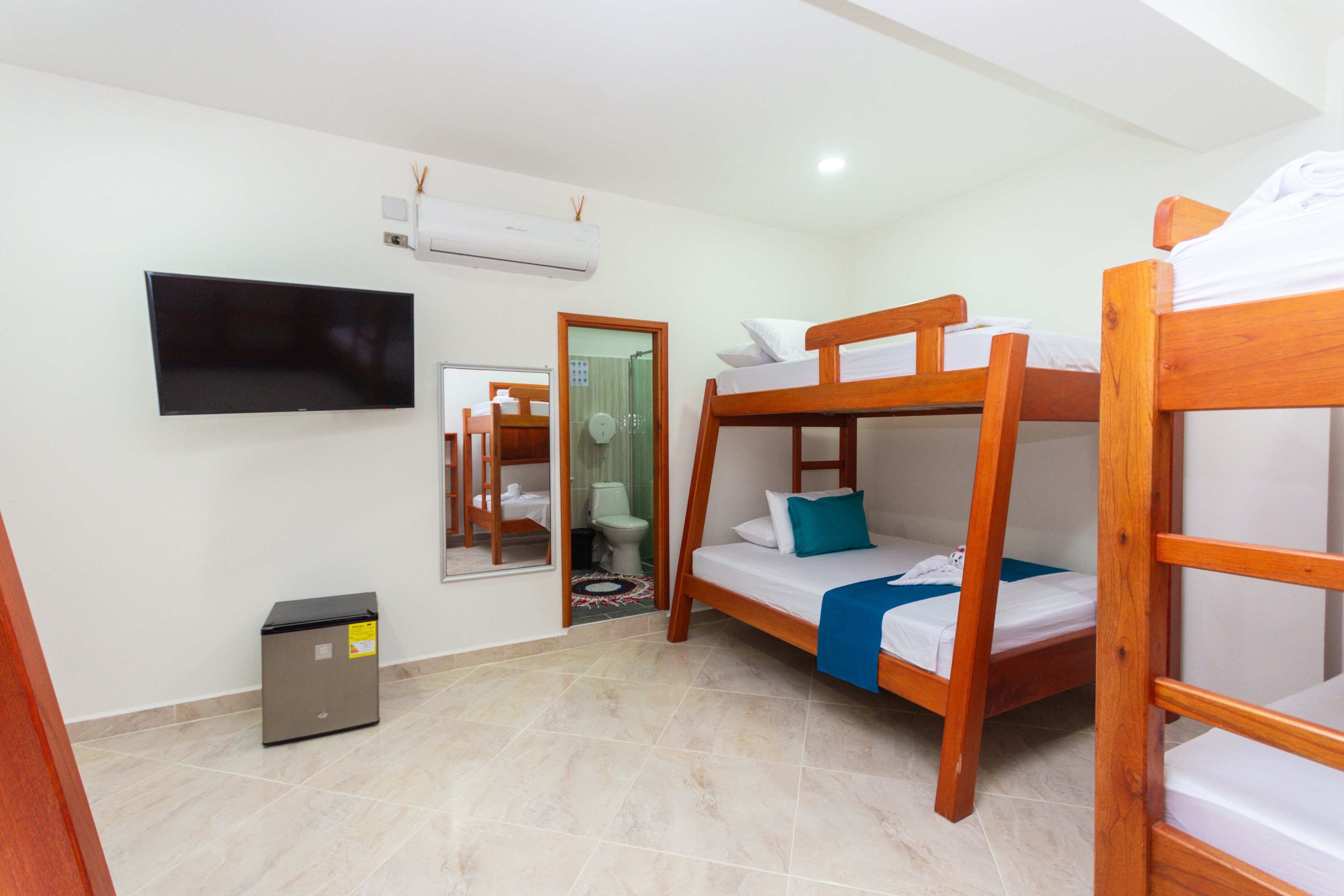 Una habitación con literas, televisor, aire acondicionado y un pequeño cubo de basura.