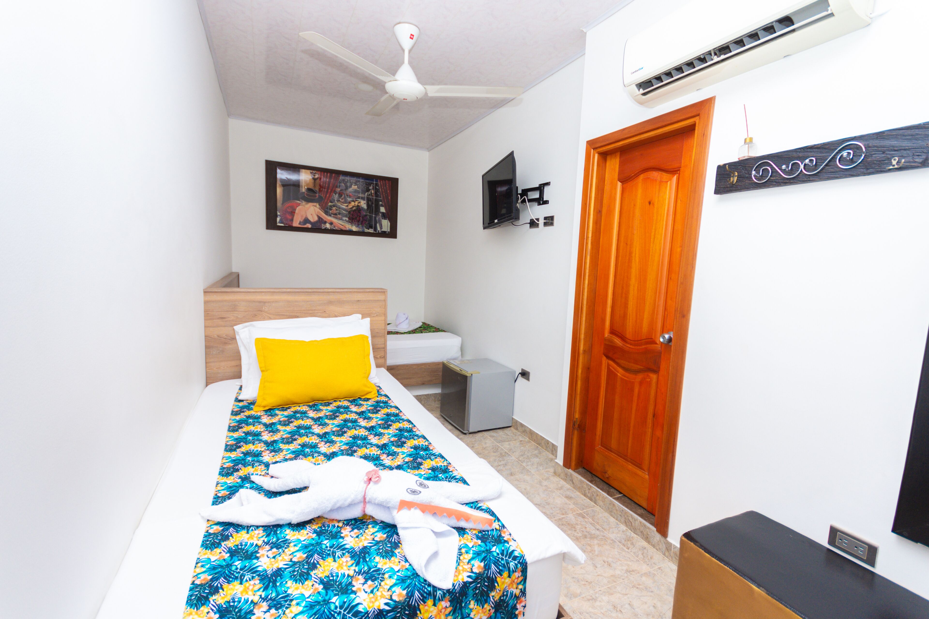 Quarto com cama, cabeceira de madeira, TV na parede, porta e ar-condicionado.