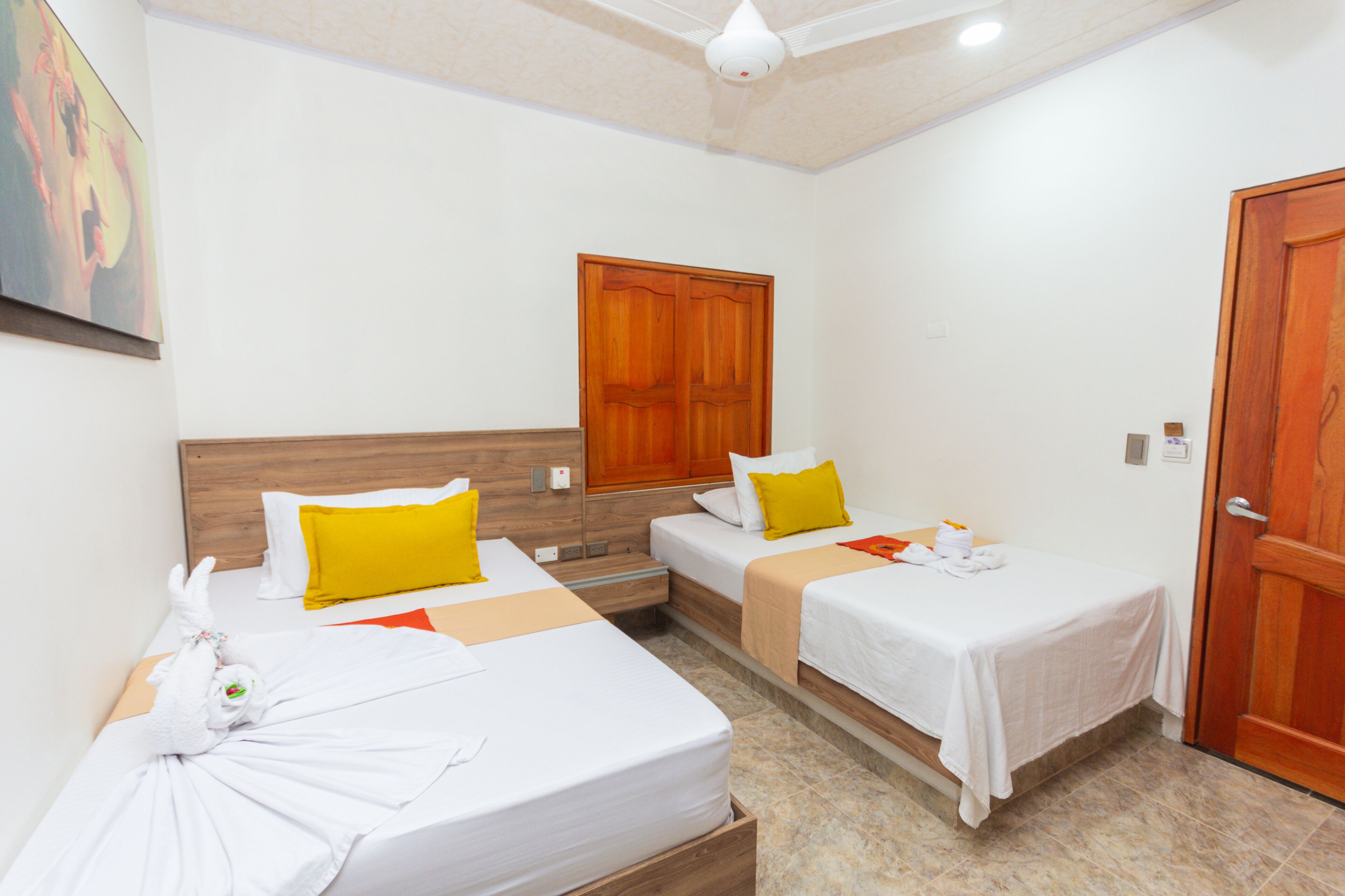 A hotel room with two single beds, a wooden wardrobe, a ceiling fan, and a door.