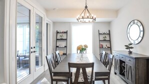 Une salle à manger avec une longue table, des chaises, un lustre et une horloge au mur.