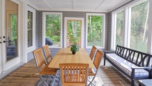 Un espace repas abrité, avec une table et des chaises en bois, de grandes fenêtres et un banc.