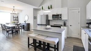 Une cuisine moderne avec des meubles blancs, un îlot central et un coin repas agrémenté d’un lustre.