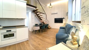 A modern kitchen with white cabinets, a built-in oven, and a dining area with a table and chairs. A staircase with a wooden railing leads to an upper level. - CATEDRAL CERVANTES 5 COLLECTION (Toledo)