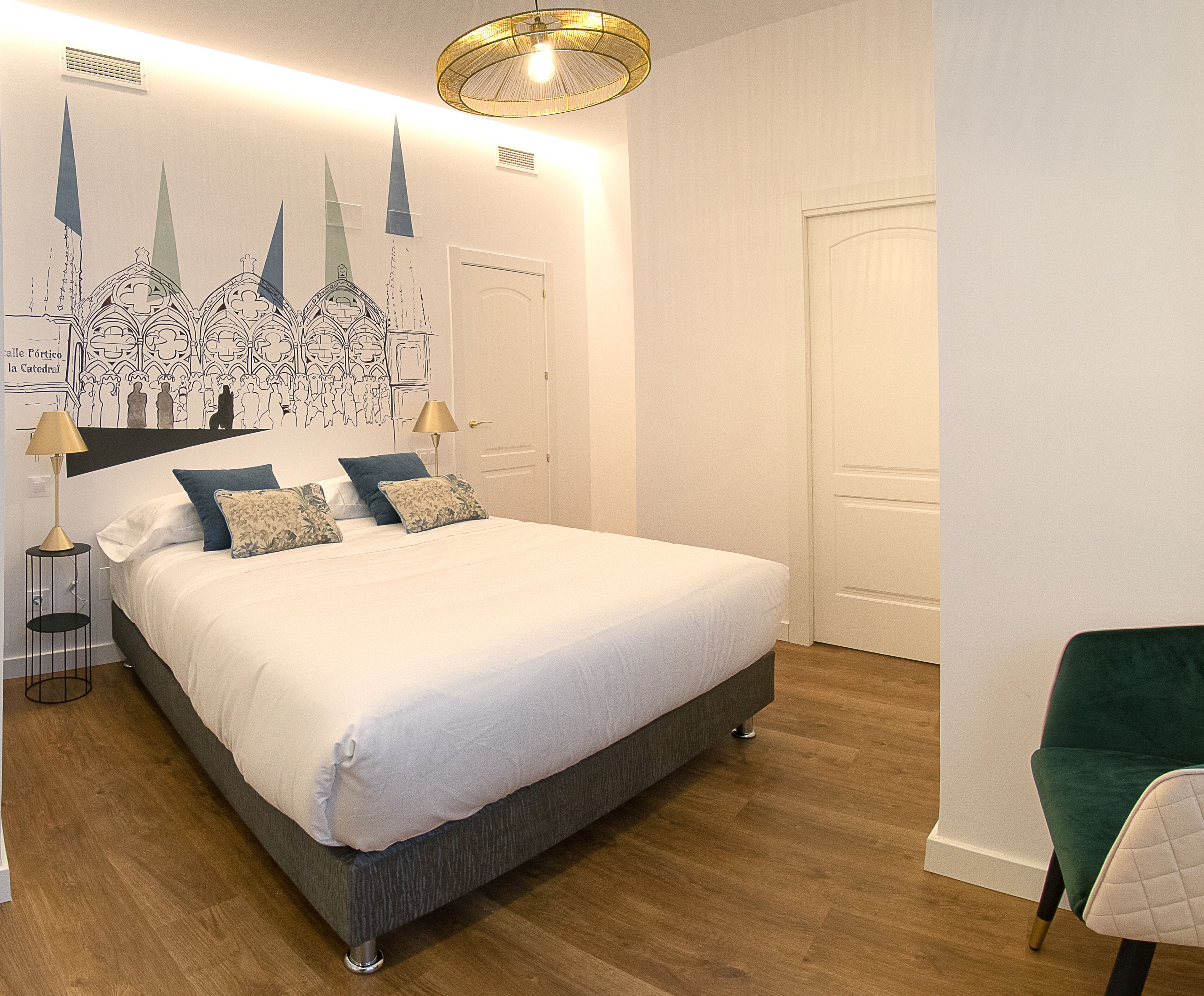 Un dormitorio con una cama grande, una mesita de noche con lámpara, una silla y un mural en la pared.