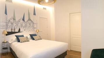 Un dormitorio con una cama grande, una mesita de noche con lámpara, una silla y un mural en la pared.