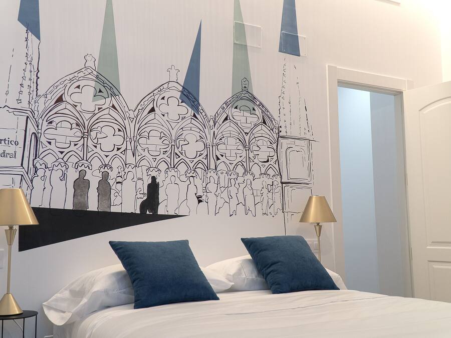 Un dormitorio con una cama, dos almohadas azules, dos lámparas de noche y un mural en la pared con un paisaje de una catedral.