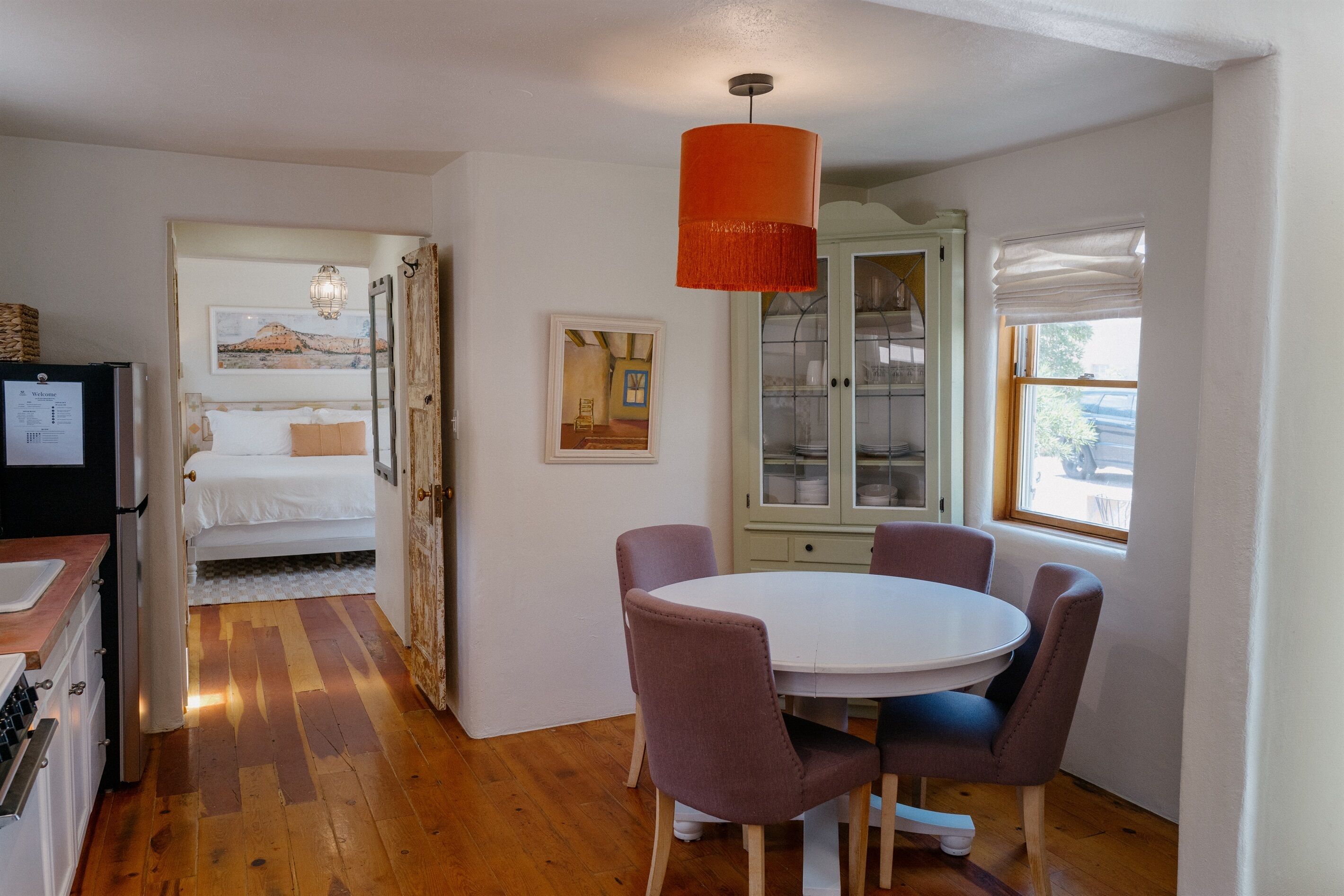A cozy room with a bed, a dining table with chairs, a kitchen area, and a window with a view.