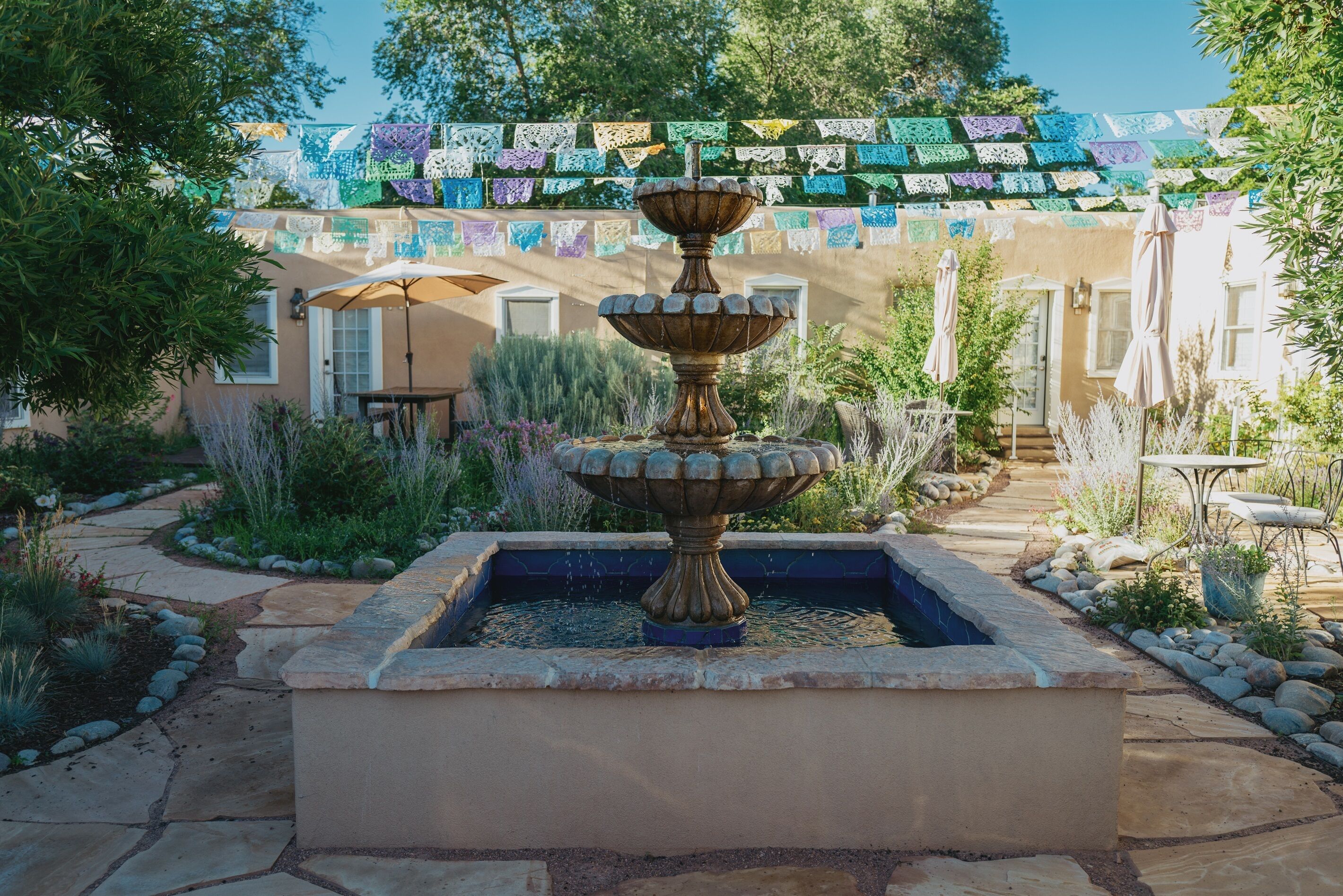 Une fontaine à plusieurs niveaux dans un jardin, avec un espace patio et un bâtiment en arrière-plan.