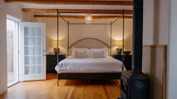 A bedroom with a four-poster bed, wooden beams, a fireplace, and a glass door leading outside.