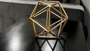 Ein modernes Interieur mit einem geometrischen Goldtisch, einem grauen Sofa und einem Fenster mit Vorhängen.