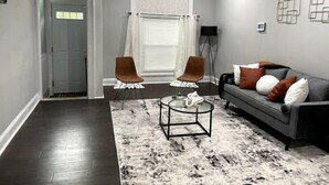 Ein modernes Wohnzimmer mit dunklem Holzboden, einem grauen Sofa mit braunen Kissen, zwei braunen Sesseln, einem Couchtisch und einer Stehlampe.