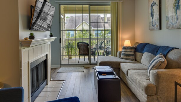 A living room with a fireplace, a sofa, a coffee table, and a view through a glass door to the outside.