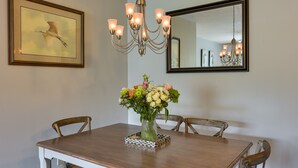A dining area with a wooden table, chairs, a chandelier, a mirror, and a framed artwork.