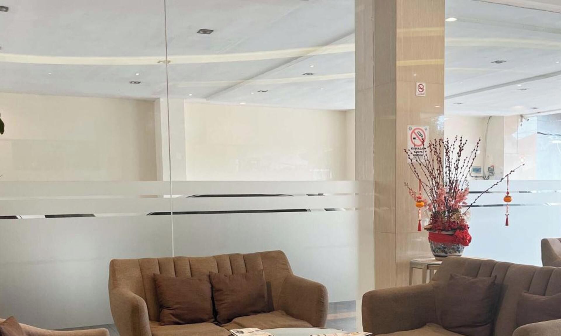 A modern lobby with a glass partition, a brown sofa, and a small table with a vase of flowers.