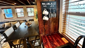 A cozy dining area with a wooden table, chairs, and a wall-mounted sign indicating the time. - Tiny House Hideaway with King sized Bed (Cape Charles)