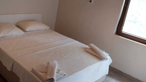 A neatly made bed with white linens and pillows, a rolled towel on the bed, and a window on the right side. - Uyku Vadisi Otel (Milas)