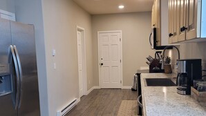 A modern kitchen with a stainless steel refrigerator, wooden flooring, and light-colored cabinets.