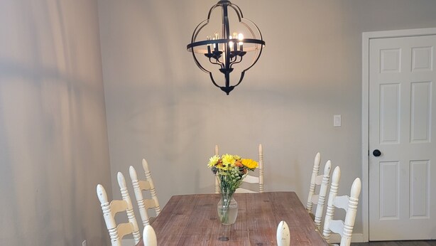 A dining room with a wooden table, white chairs, a chandelier, and a vase with flowers.