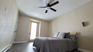 A bedroom with a bed, a ceiling fan, a door, and a window.