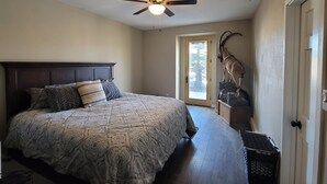 A bedroom with a large bed, a ceiling fan, a door with a view, and a mounted animal head.